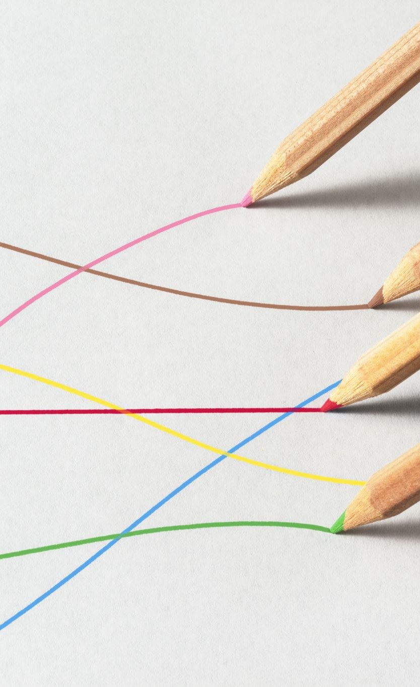 Colored pencils resting on white paper, each one at the end of the line it has drawn.